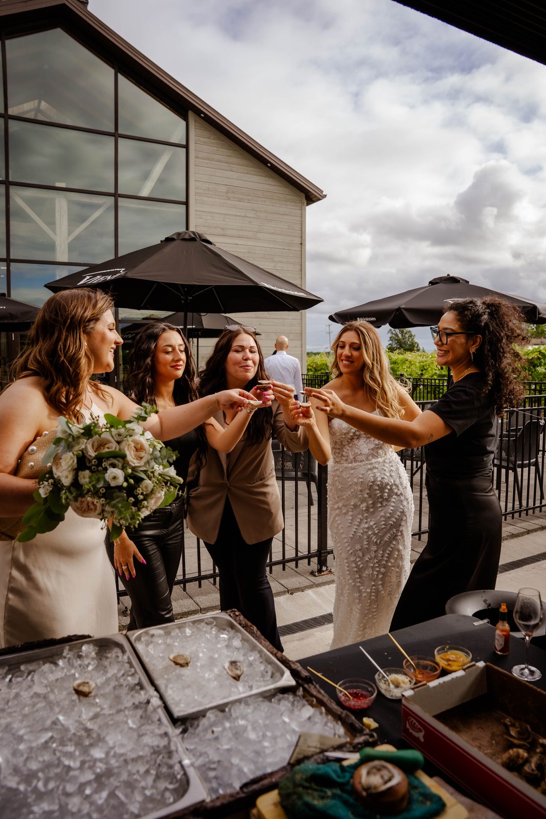 A bride and her bridesmaids cheers with fresh oysters at the raw bar during cocktail hour