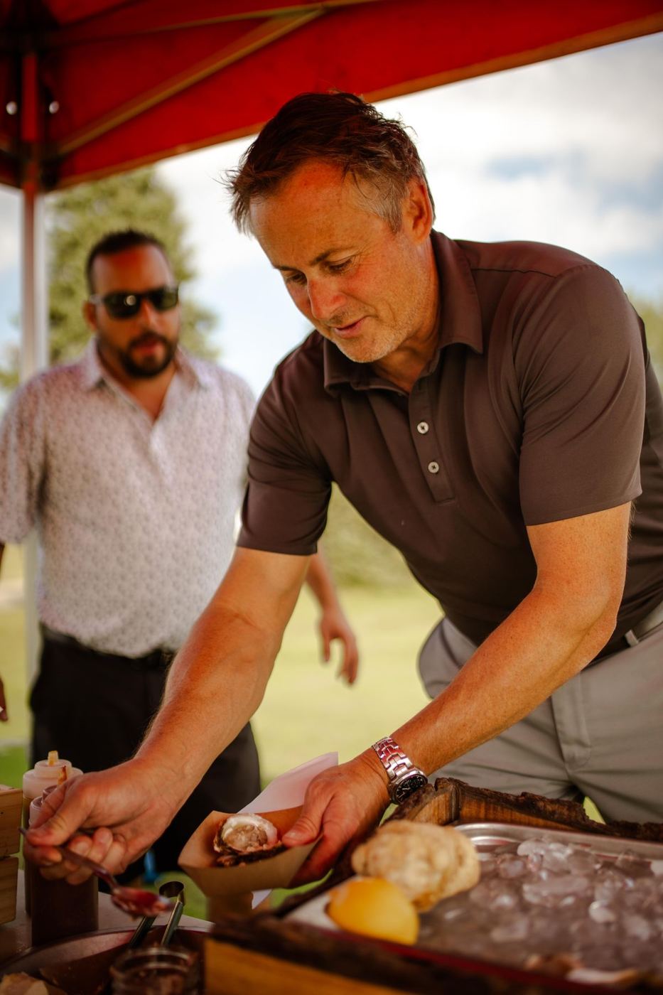 A guest shucking an oyster at the raw bar under a tent at a corporate golf tournament