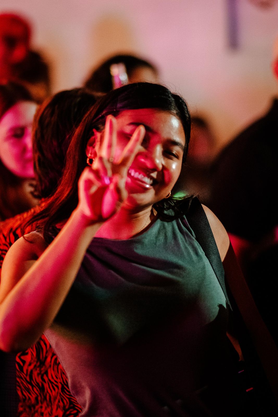 A guest throwing a peace sign in pink light at Art Crawl