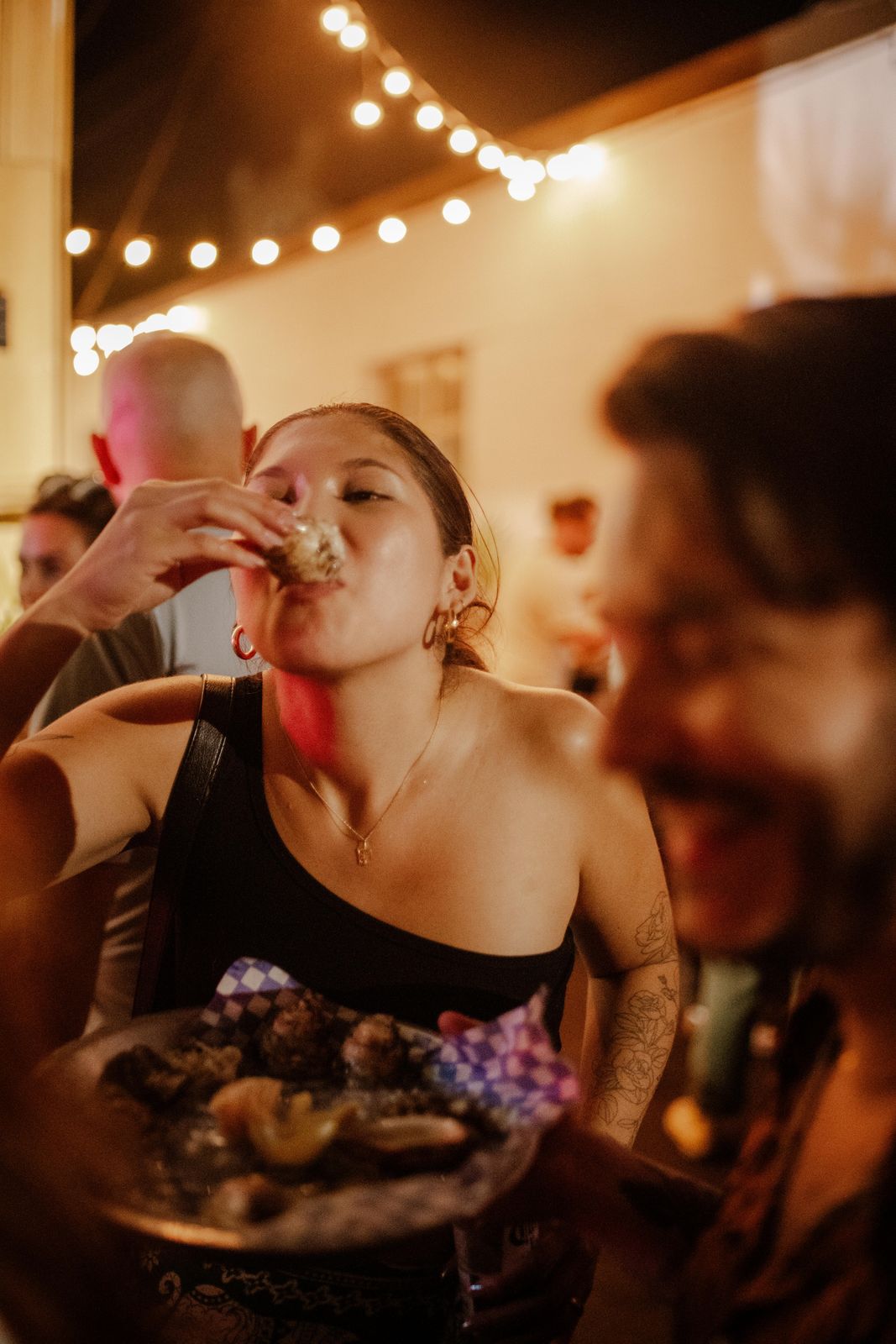 A guest slurping an oyster under string lights at Art Crawl
