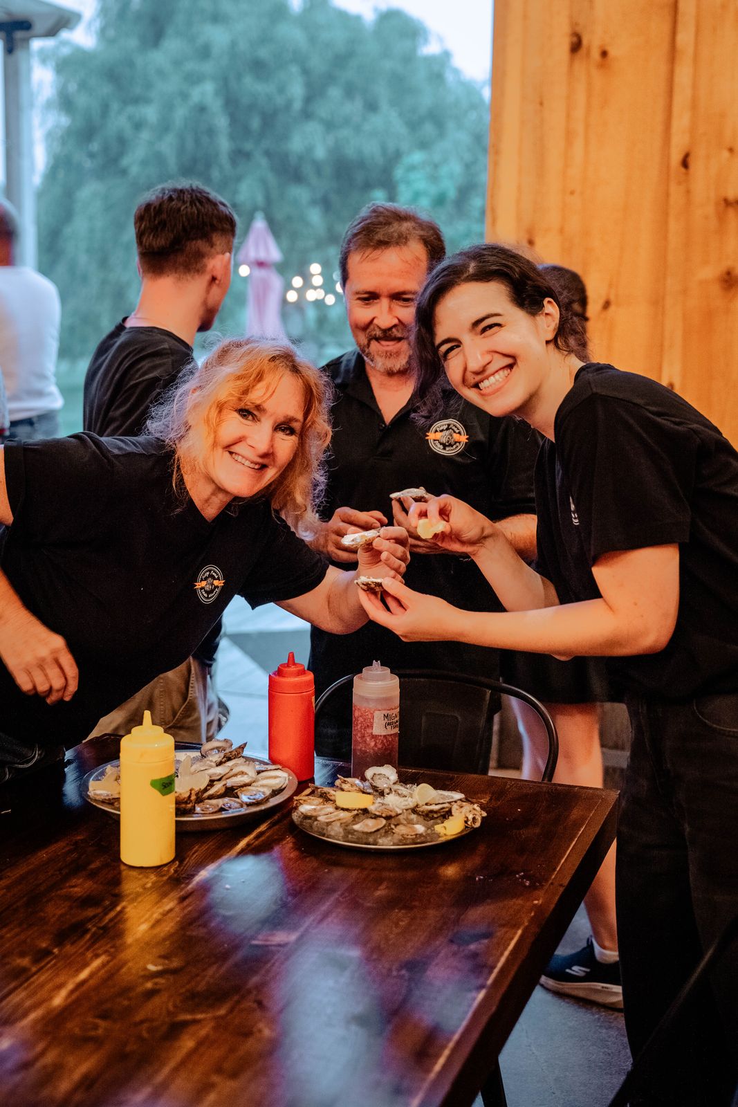 Staff and a guest laughing over oysters at a wooden bar