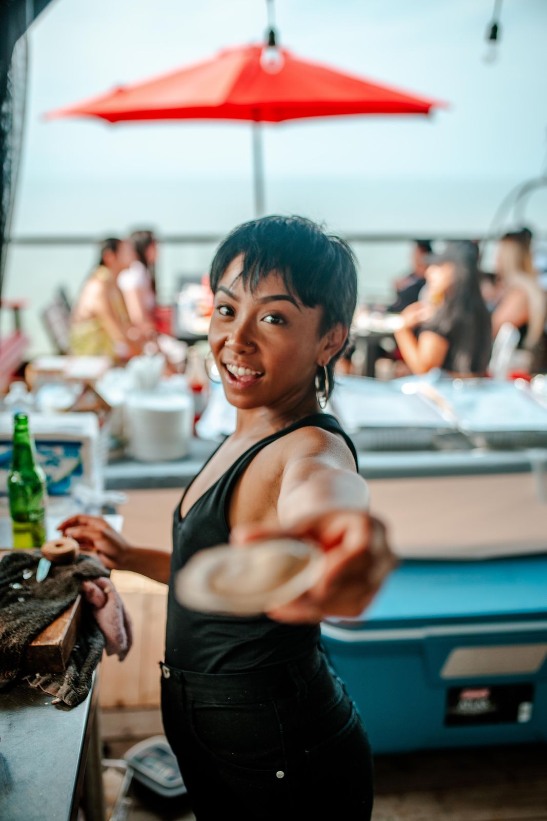 A shucker handing out a fresh oyster on a summer patio