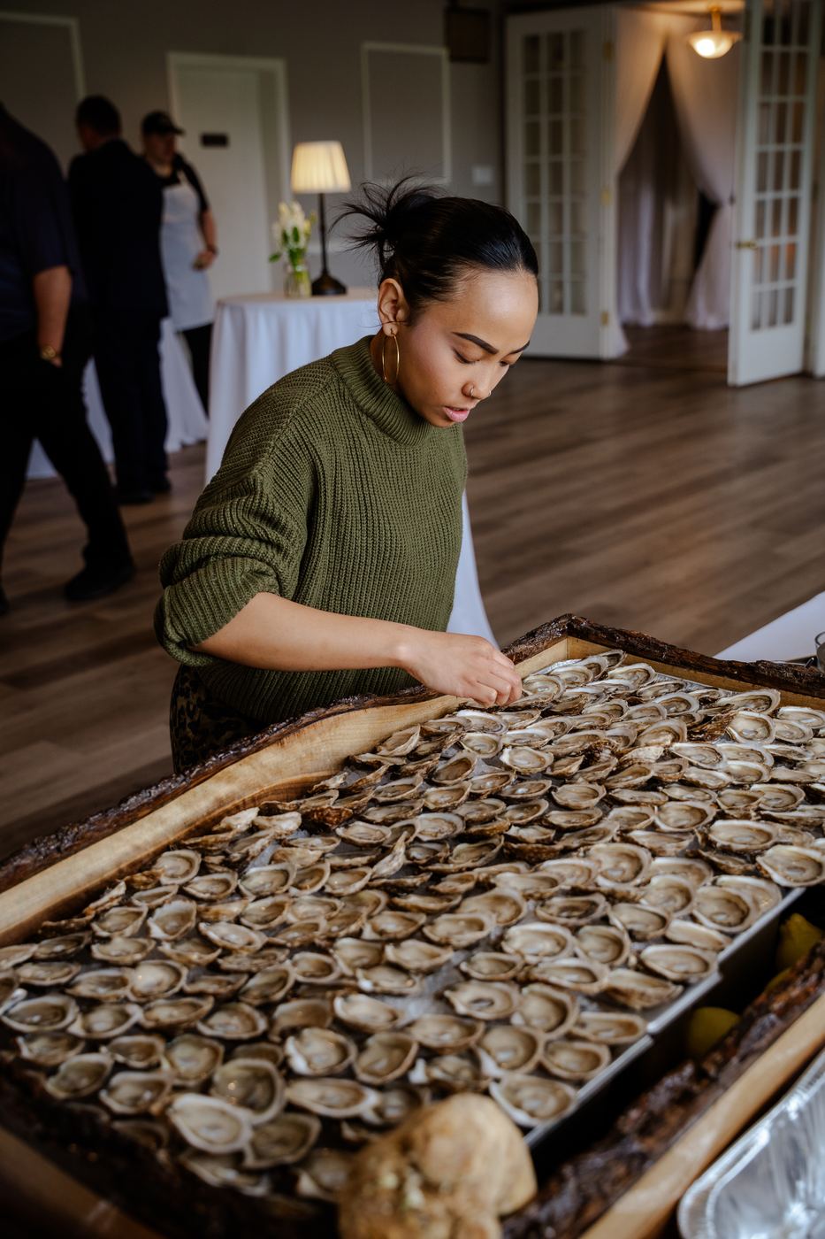 A shucker arranging oysters across the long live-edge board at a venue