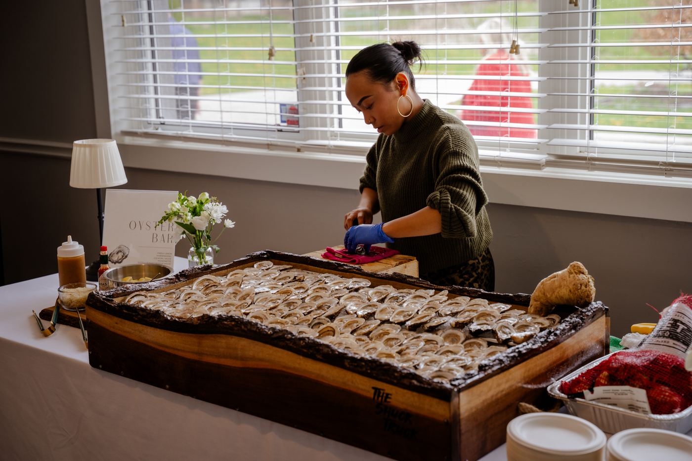 The live-edge board loaded with oysters on a white tablecloth beside a window