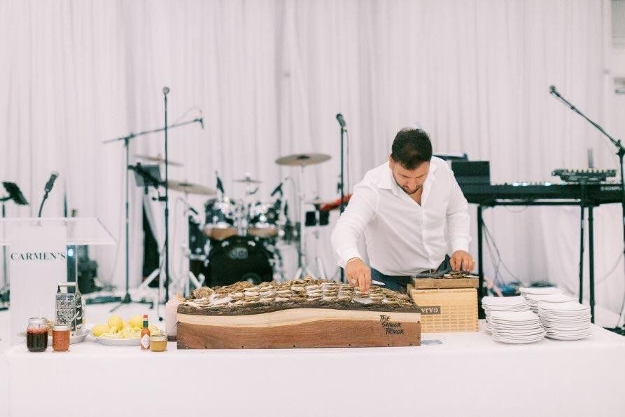 The live-edge board set up on a white-draped table at a wedding reception, with the band stage behind