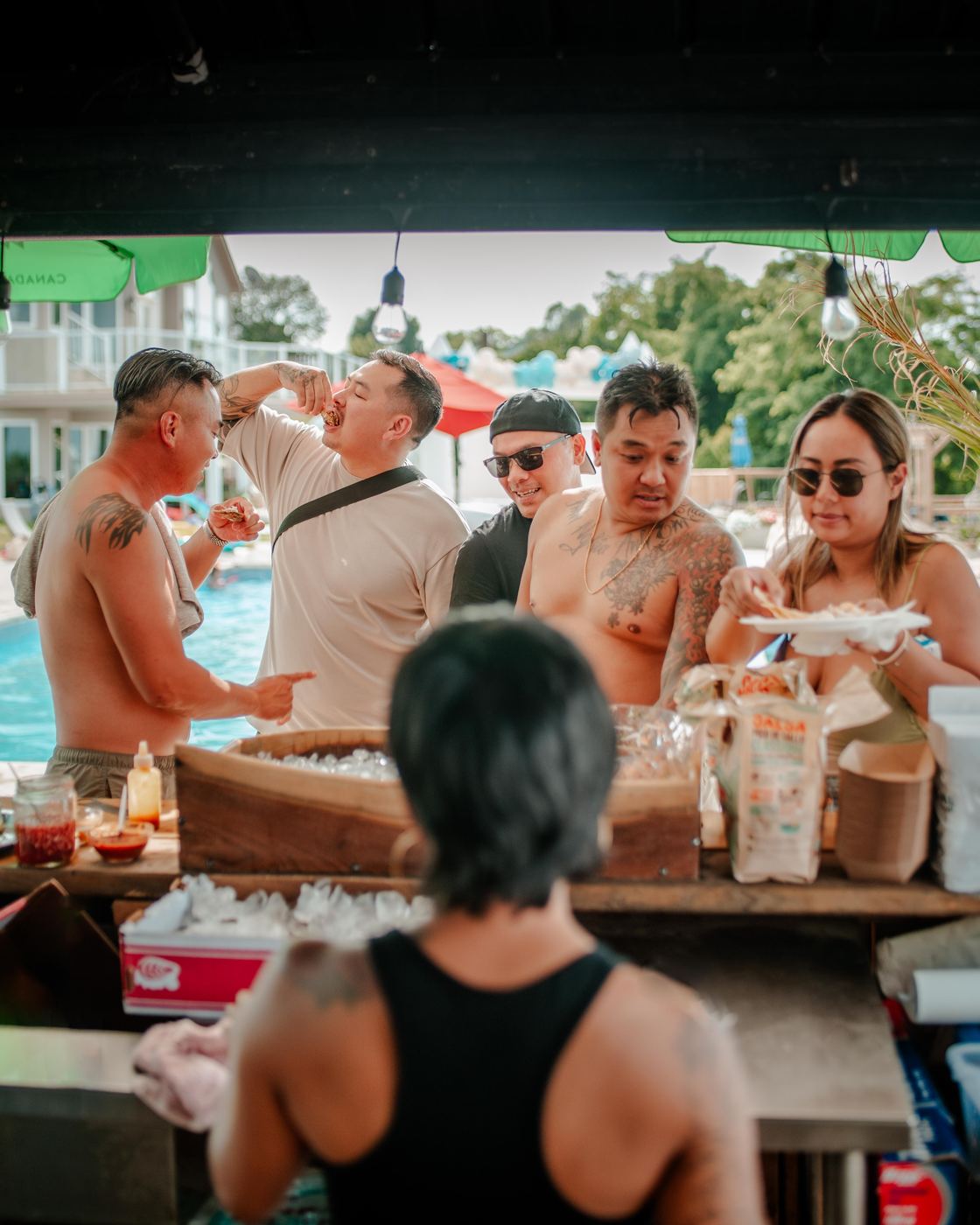 Friends at a pool party tipping back oysters at the raw bar