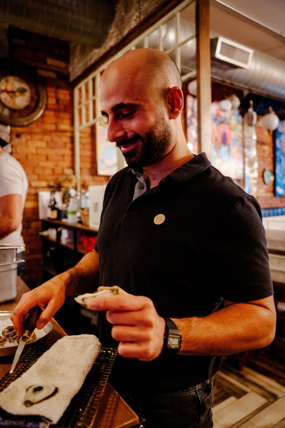 Ramsen Slewa shucking an oyster, wearing his Oyster Master Guild pin