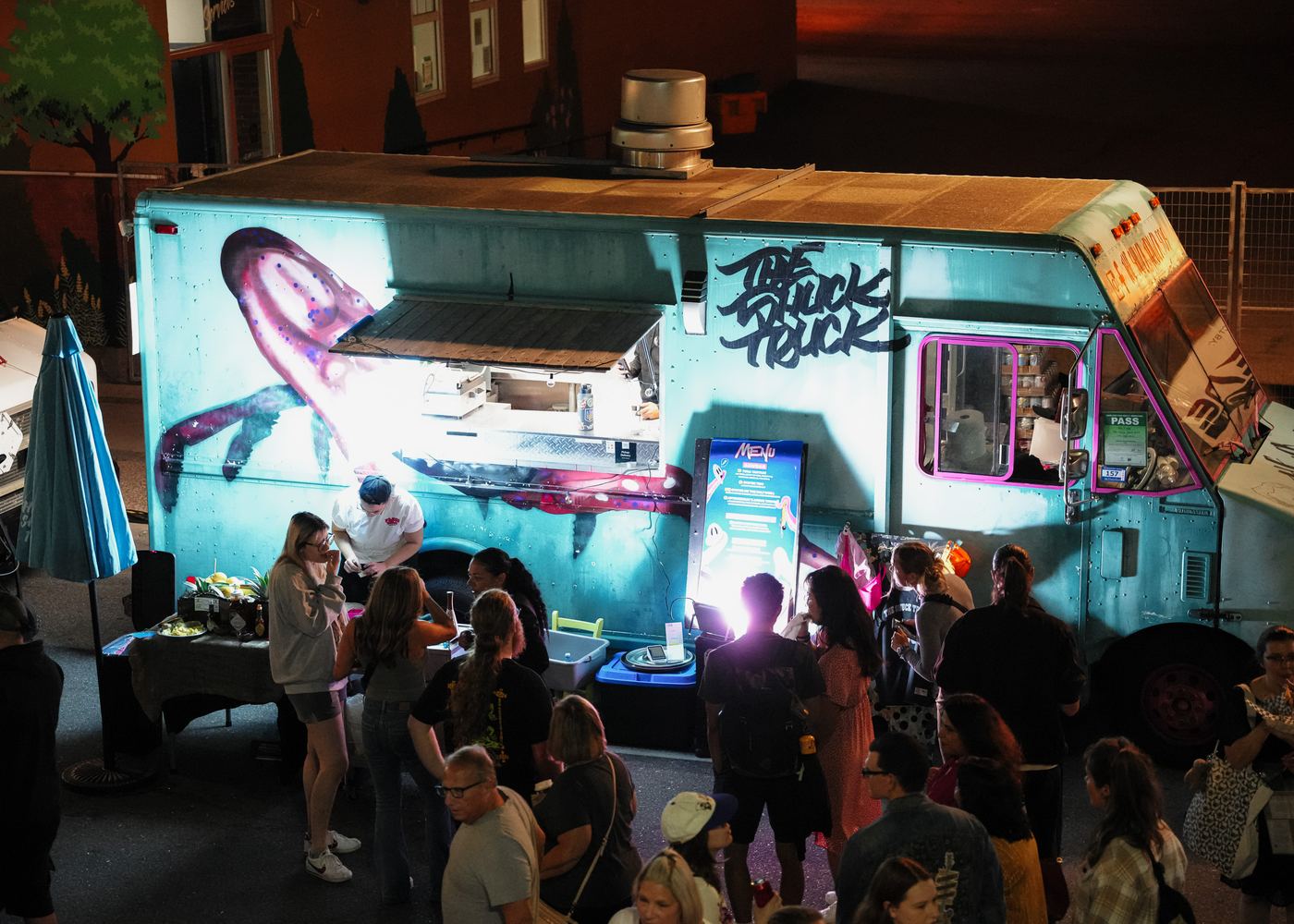 The Shuck Truck lit up at night with a crowd gathered at the window on Locke Street