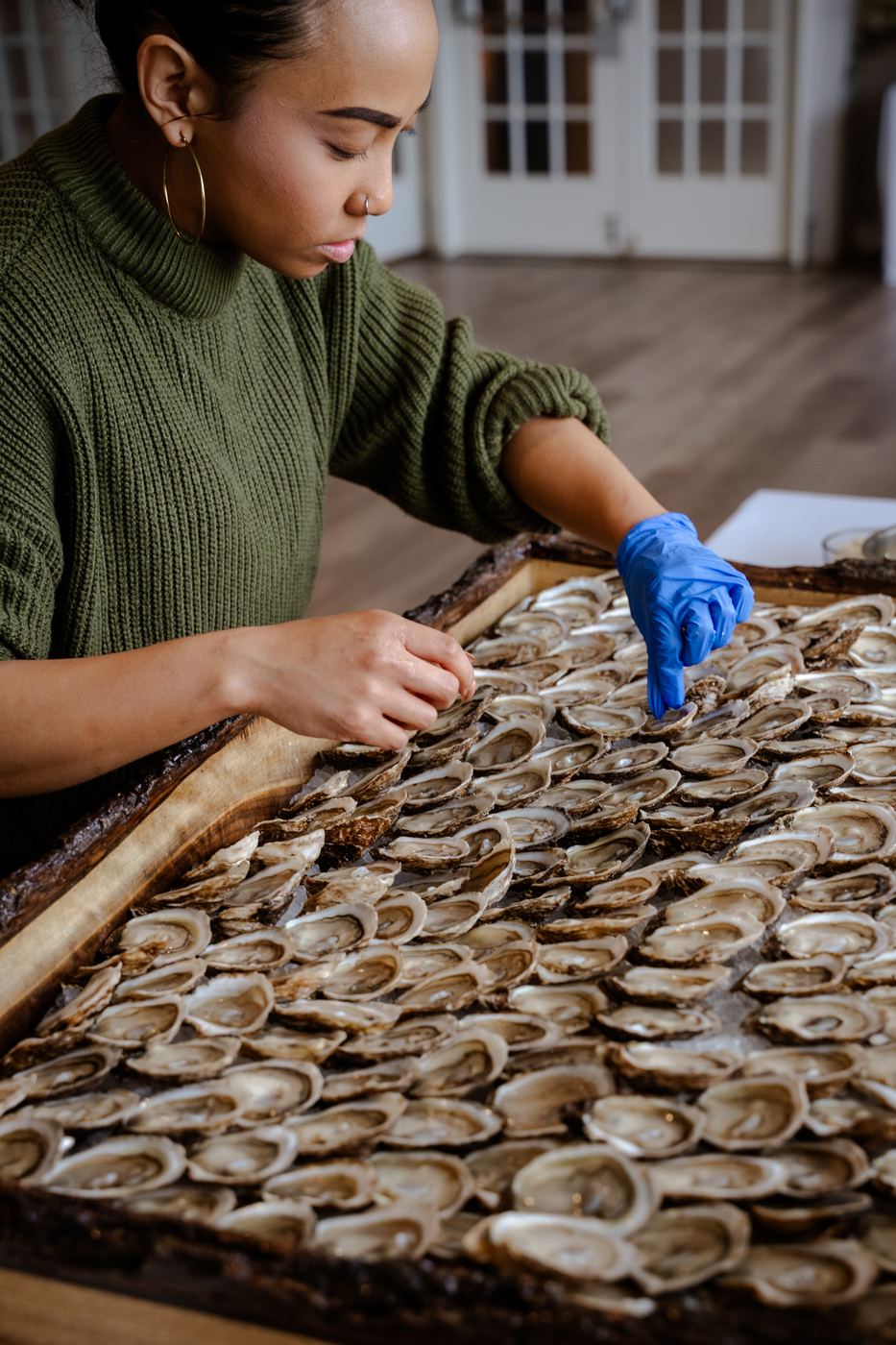 A shucker in a gloved hand opening an oyster over the live-edge board